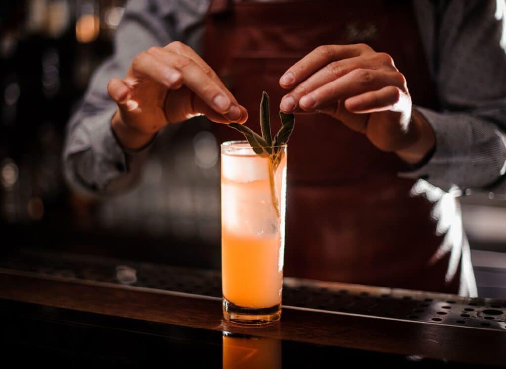Hands garnishing cocktail with rosemary. 