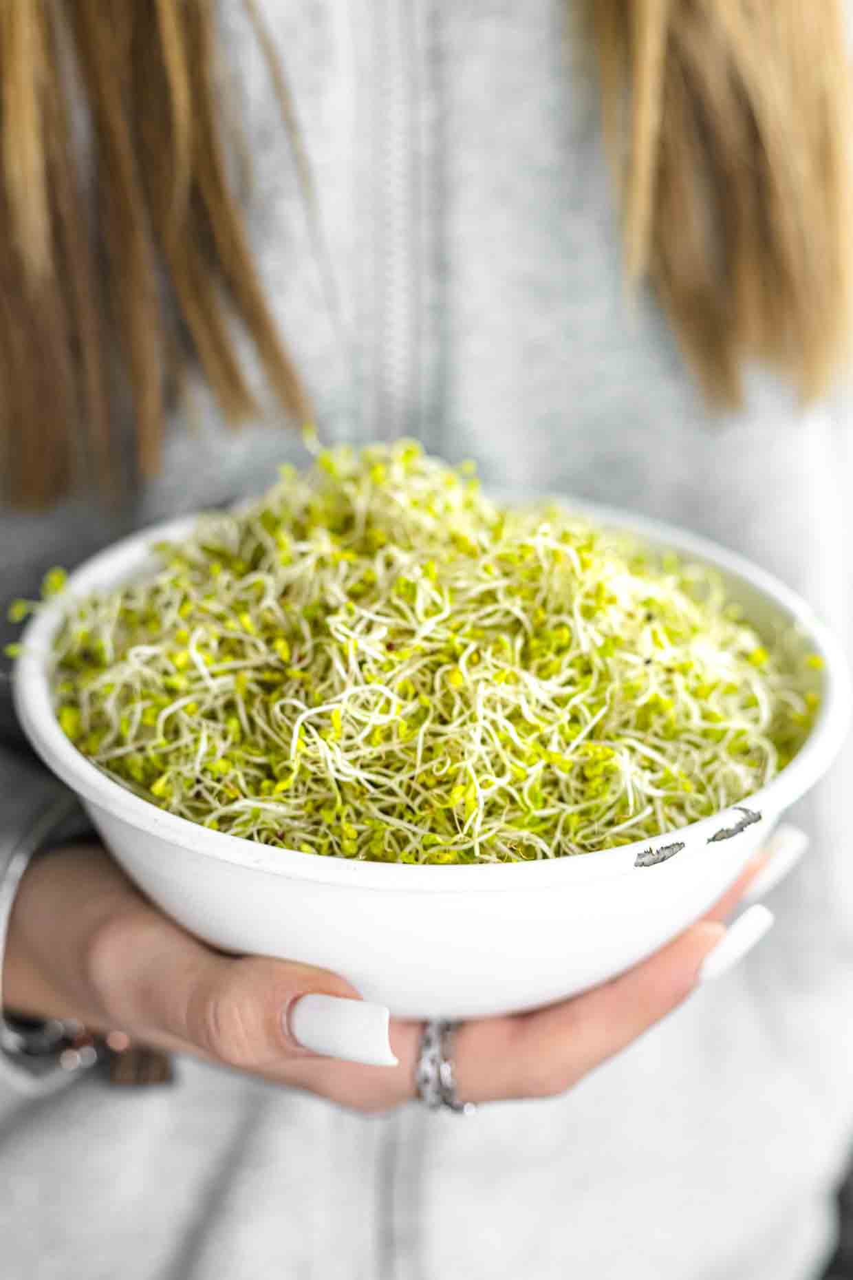 A girl holding a bowl of sprouted broccoli seeds.