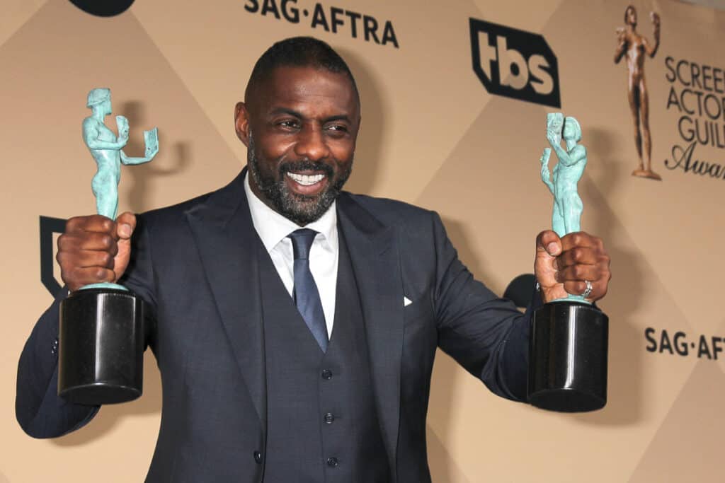 Idris Elba holding up his awards.