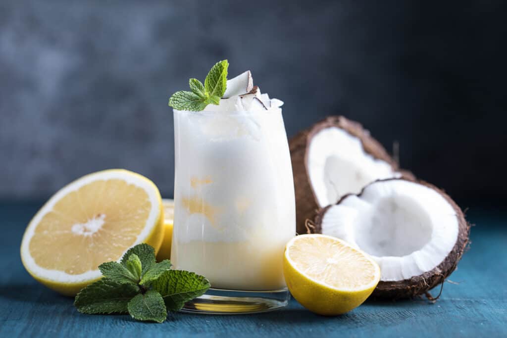 A pina colada cocktail next to coconuts and lemons.