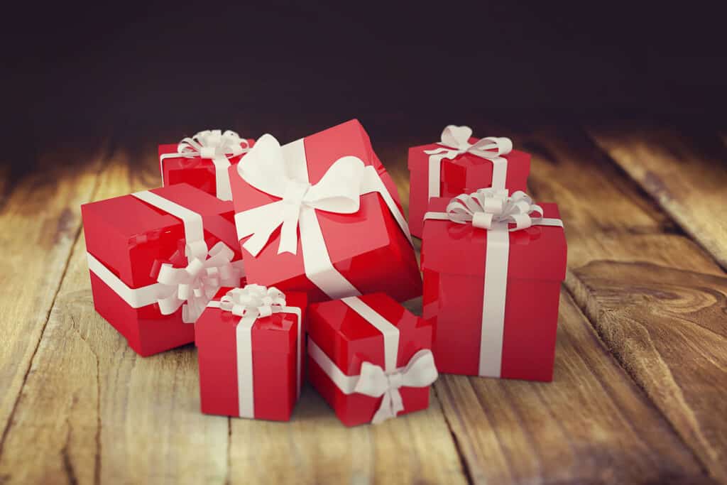 Seven red gift boxes with white ribbons and bows arranged on a wooden surface with a dark background.