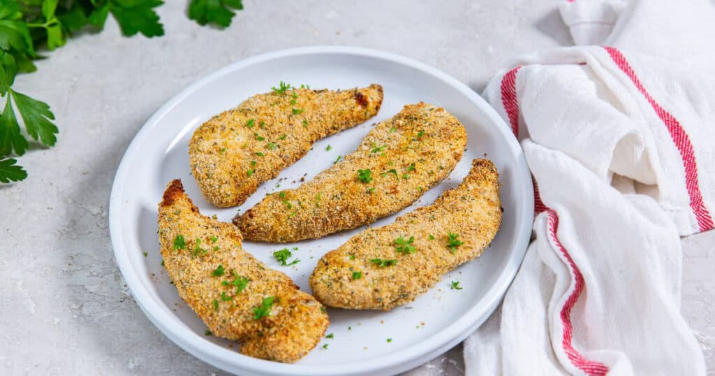 4 breaded chicken tenders on a white plate with a napkin