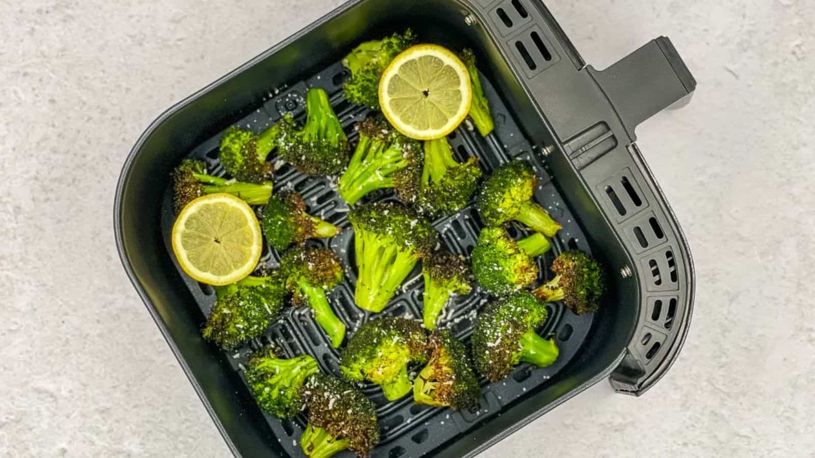 An air fryer basket with broccoli and lemon slices in it.