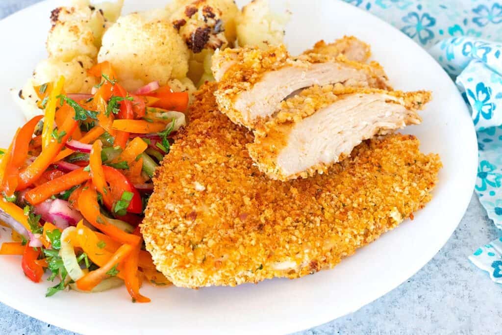 Air Fryer Chicken Cutlets on a white plate with bell pepper salad and roasted cauliflower.
