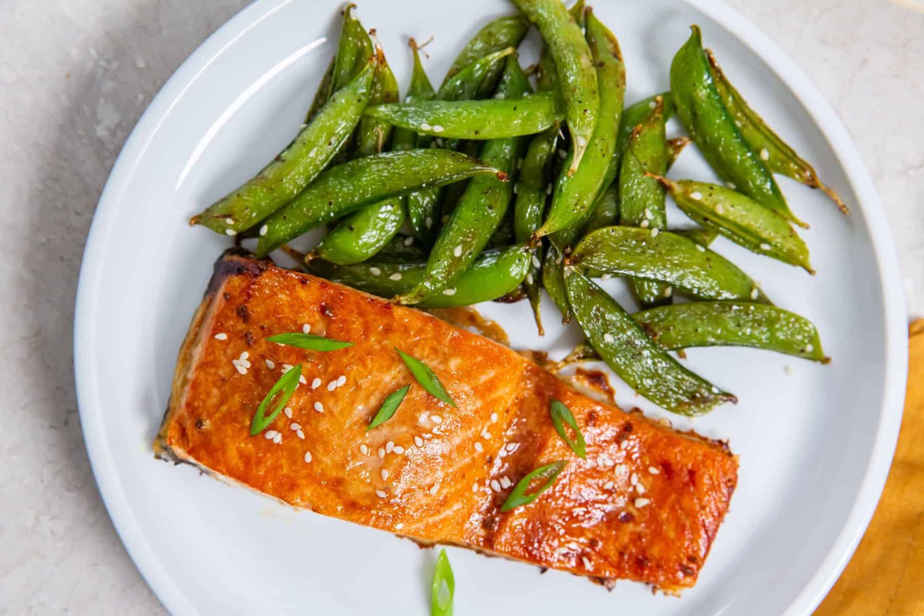 Air Fryer Salmon on a white plate with sugar snap peas and green onions.