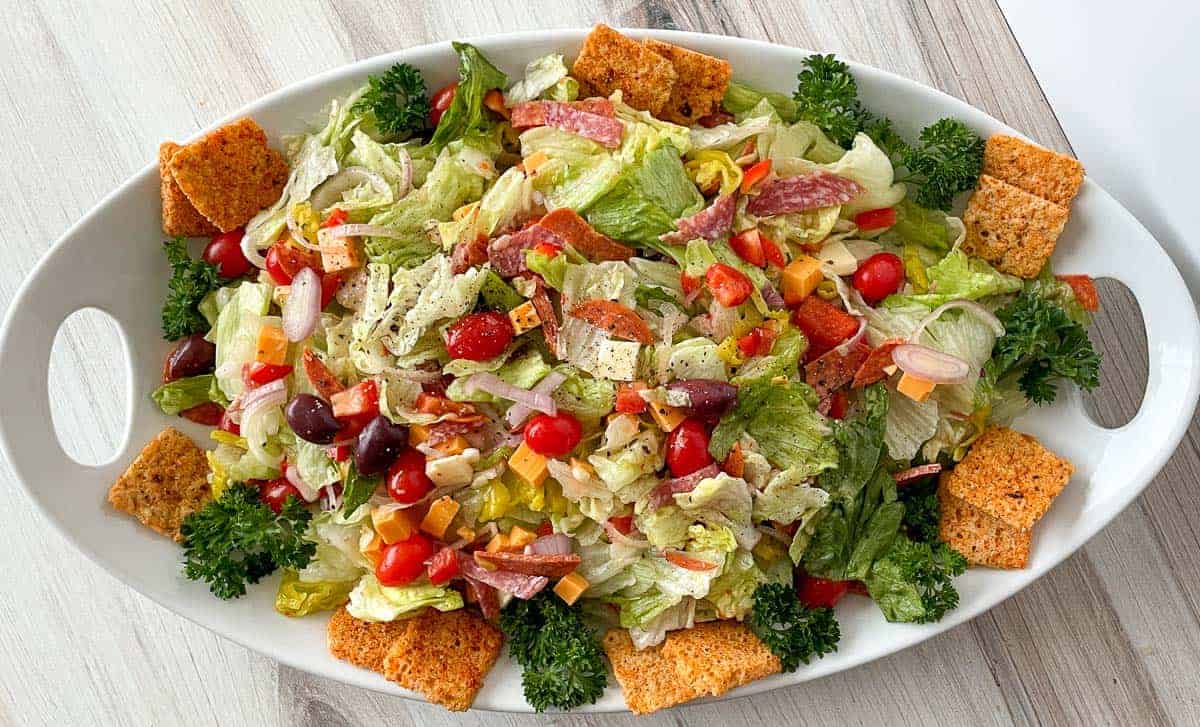 Image shows an overhead view of an Antipasto Salad in a white bowl.