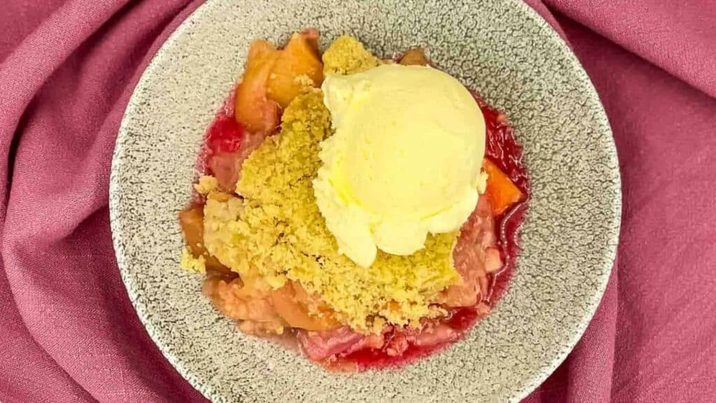 Top down shot of apple rhubarb crumble in a bowl with a scoop of ice cream.