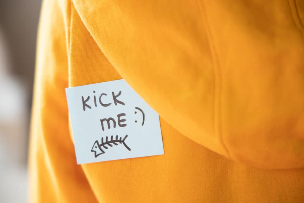 Sticky paper on yellow with text KICK ME and fish on back, closeup. April fools day concept.