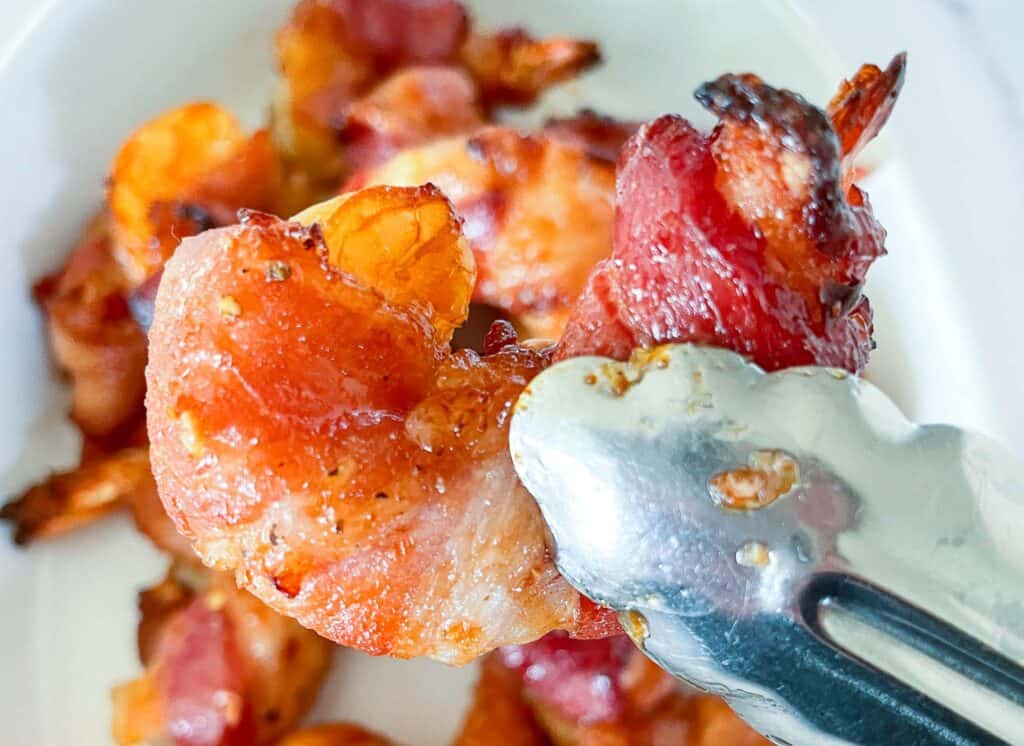 Bacon wrapped shrimp held by tongs. 
