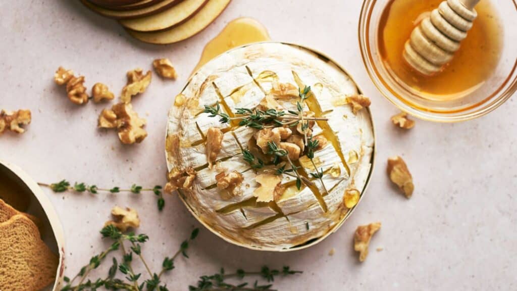 A baked brie with walnuts and thyme, with a jar of honey next to it.