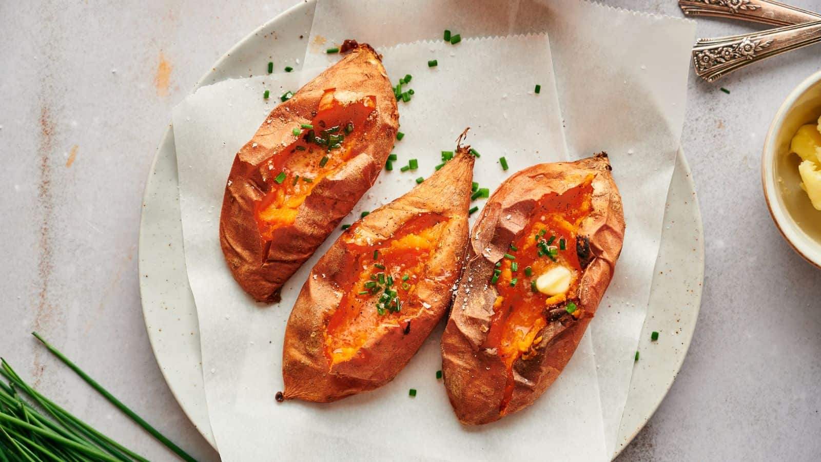 Three roasted sweet potatoes on a plate with chives.