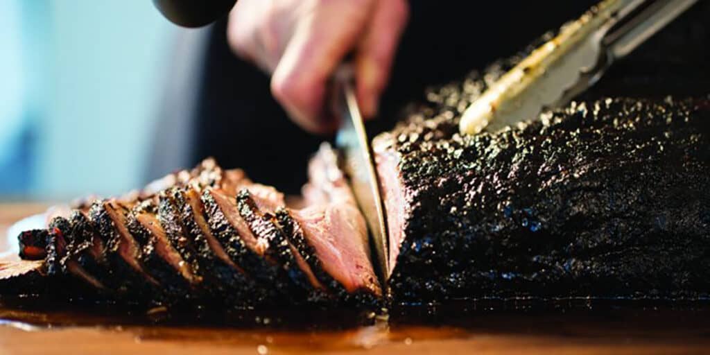 A smoked beef brisket being cut into slices.