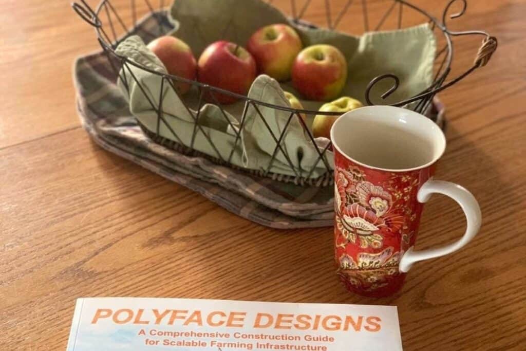 Polyface Design homestead book with a cup of tea and basket of apples.