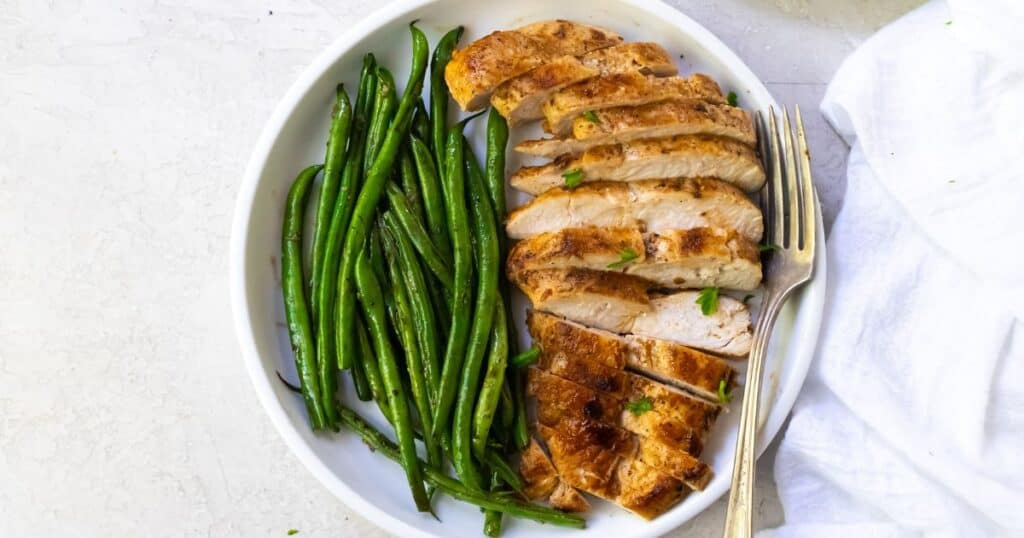 sliced blackstone chicken breast on a white plate with green beans
