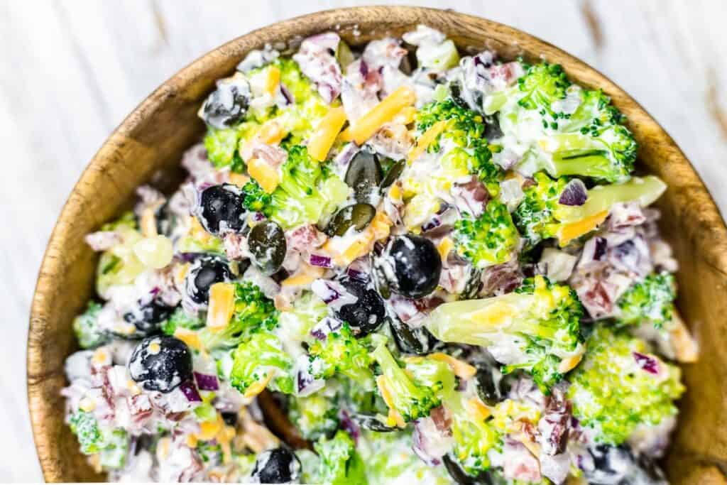 A colorful broccoli salad in a creamy dressing in a wooden bowl.