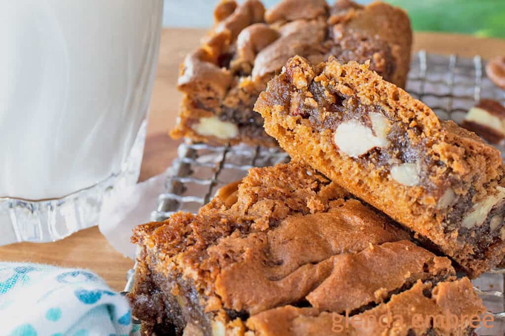 Brown Sugar Brownies cut and stacked on a wire cooling rack next to a glass of milk and a blue print fabric napkin.