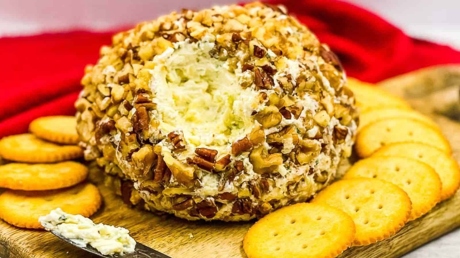 A cheese ball on a cutting board with crackers.