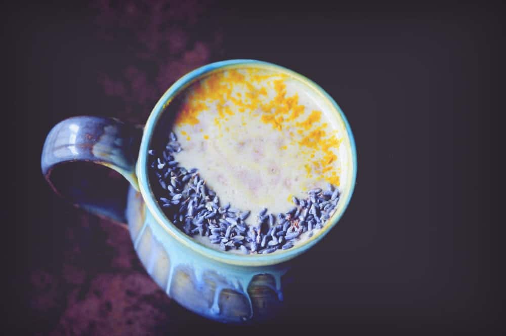 A ceramic mug filled with a white liquid topped with a yellow powder and purple flowers.