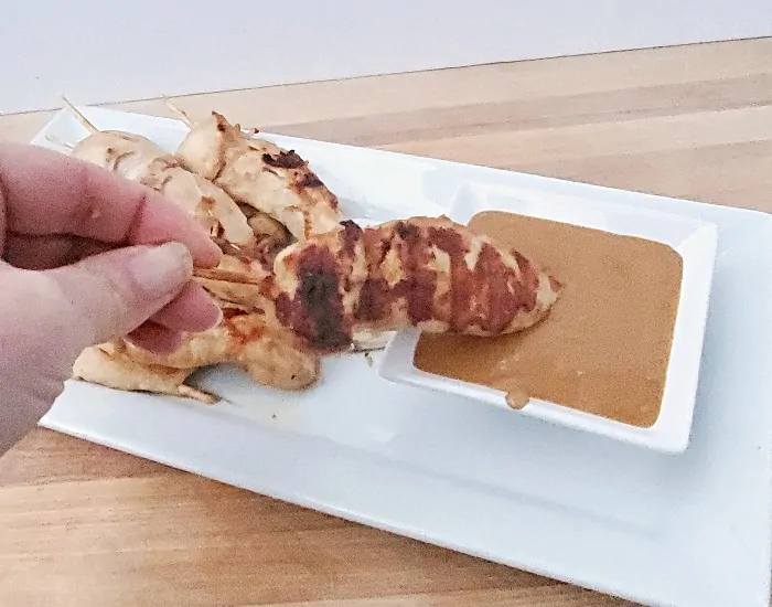 Dipping Chicken Satay into a bowl of Peanut Sauce.