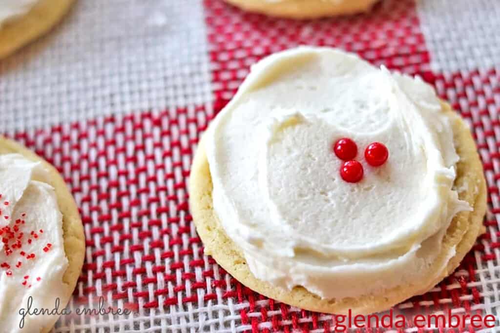 Drop Sugar Cookie with Vanilla Buttercream Icing and 3 red candy decorations. Cookies are sitting on red and white checked burlap.