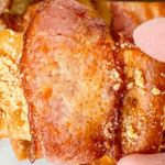 Fingers holding a bacon wrapped crackers.