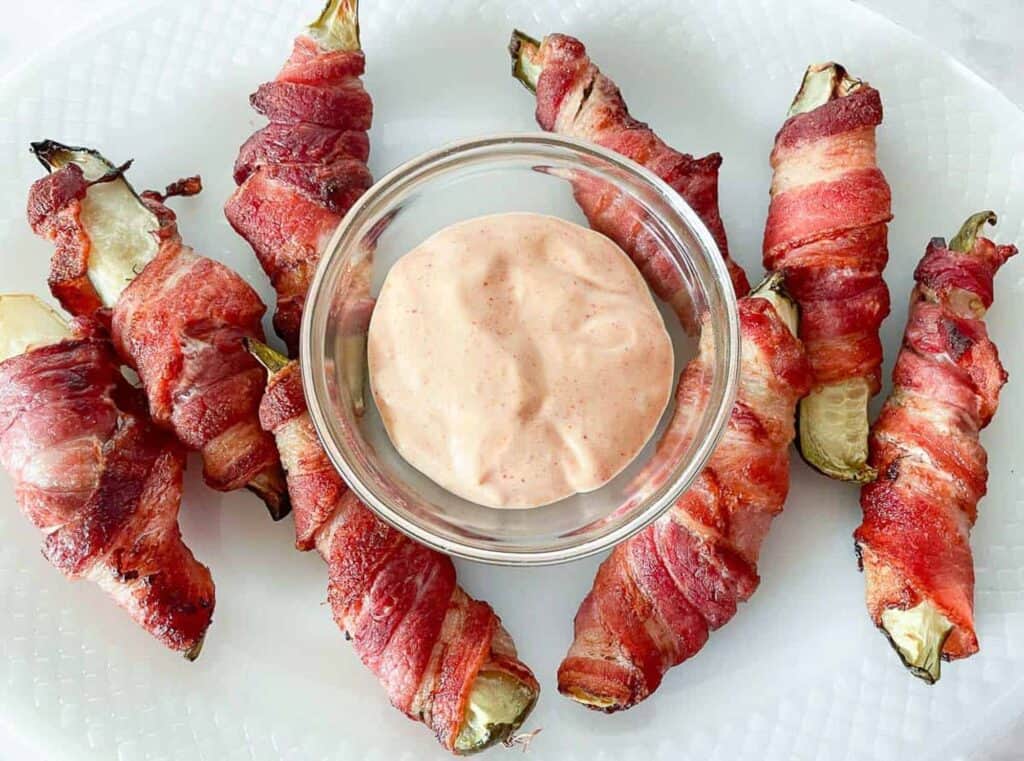 Bacon wrapped pickles with spicy mayo on a platter.