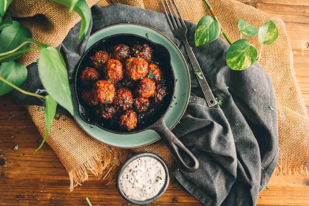 Sausage balls in cast iron skillet on a plate with linens. 