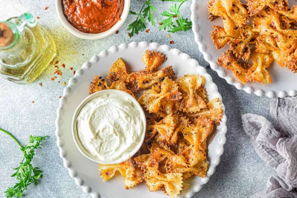 Crispy pasta chips on a plate with sauce. Another plate in the photo also hold chips.