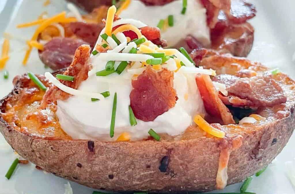 Loaded Potato Skins on a platter with cheese, sour cream, bacon, and chives.