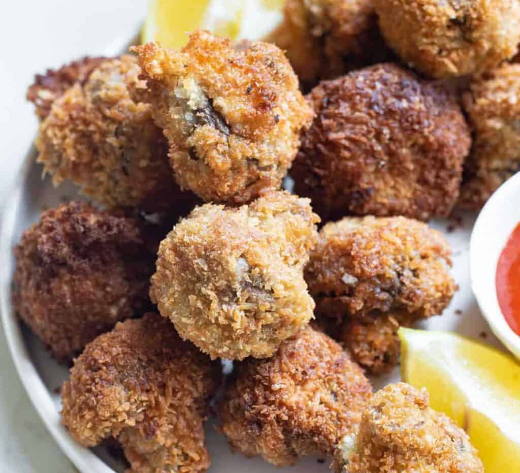 Fried mushrooms on a plate with sauce and lemon wedges.