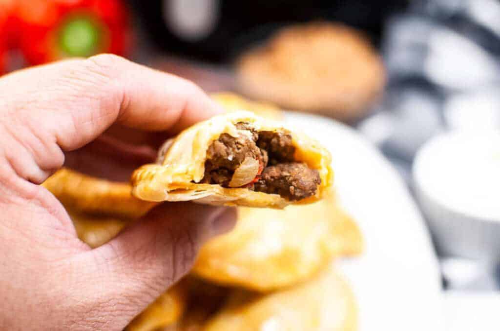 Half an empanada being held in a hand in front of a blurred background. 