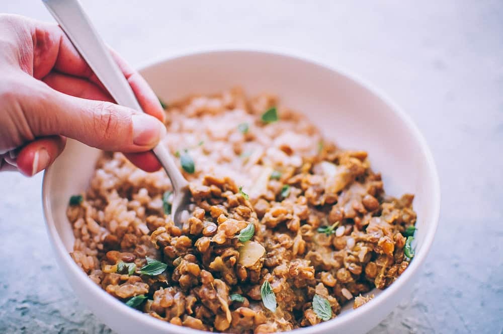 Green lentil curry in a bowl with a hand holding a spoon.