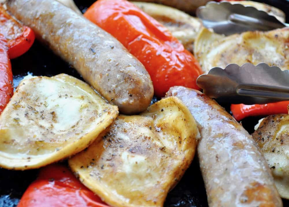 Sheet pan dinner with pierogies, peppers, and sausages with a pair of tongs in the photo. 