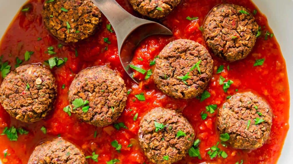 Black bean meatballs in tomato sauce in a skillet with serving spoon.