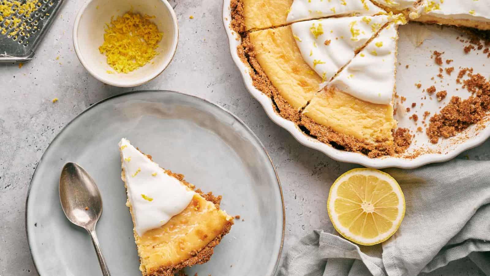 A slice of lemon pie sits on a plate next to a pie with a slice removed.
