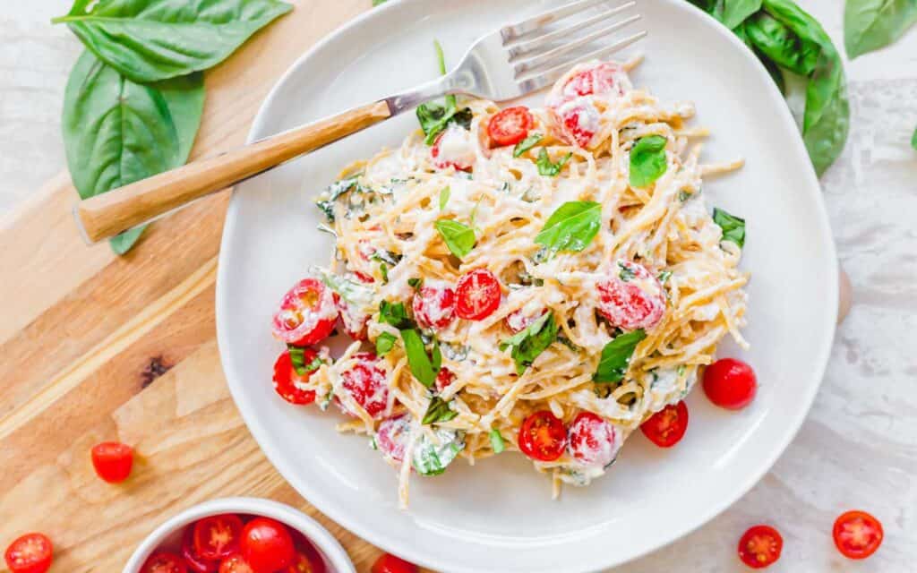 Lemon ricotta pasta with cherry tomatoes and basil on a white plate.