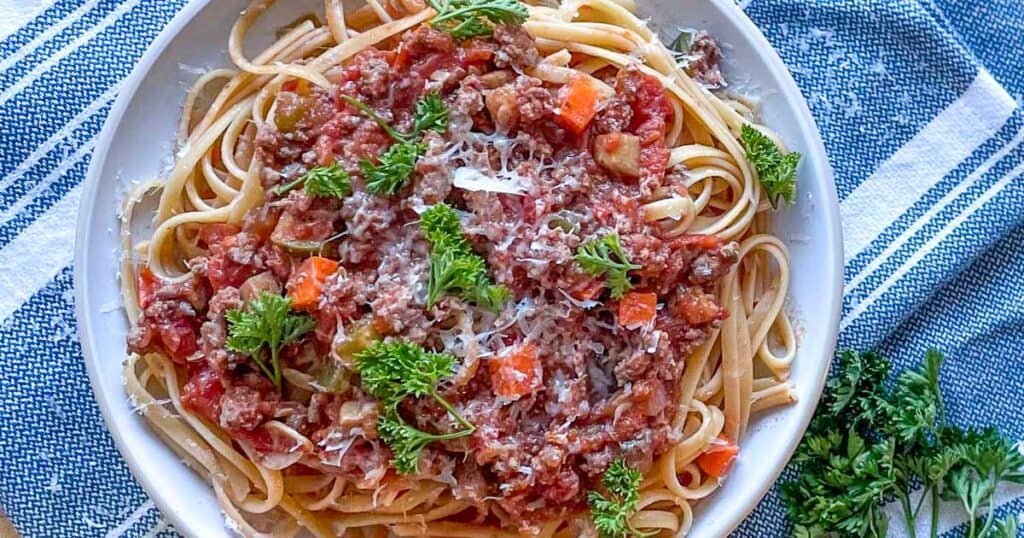 linguine bolognese on a white plate topped with parsley and parmesan.