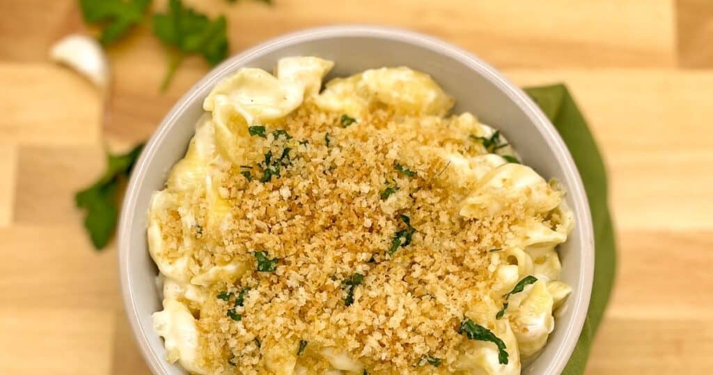 A bowl of white cheddar mac and cheese with a bread crumb topping in a white bowl.