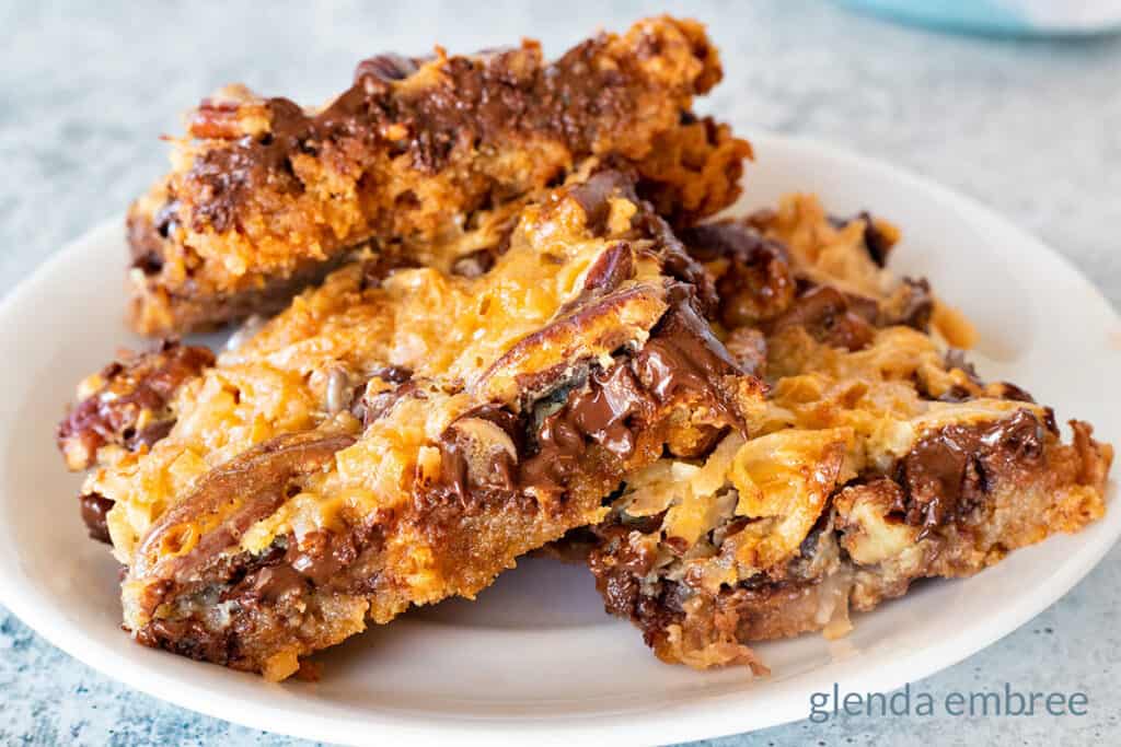 (Cookie Recipes) Magic Cookie Bars on a white plate.  The plate is resting on a concrete counter top with a turquoise and white fabric napkin in the background.