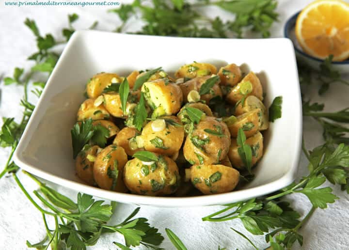 Sliced potatoes topped with herbs in a white bowl.