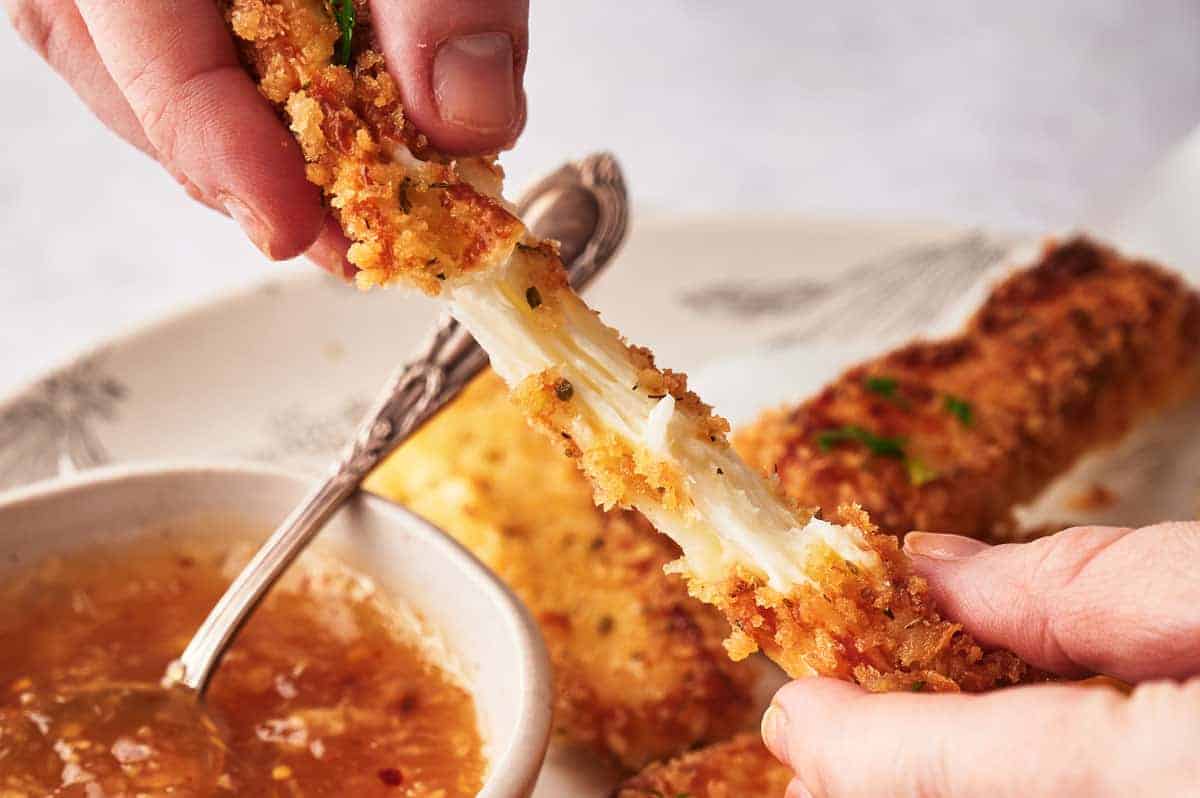 Someone pulling a mozzarella stick apart and showing the stretchy cheese.