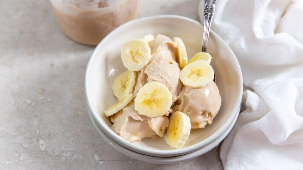 Ninja Creami Banana Protein Ice Cream in a white bowl with sliced bananas.