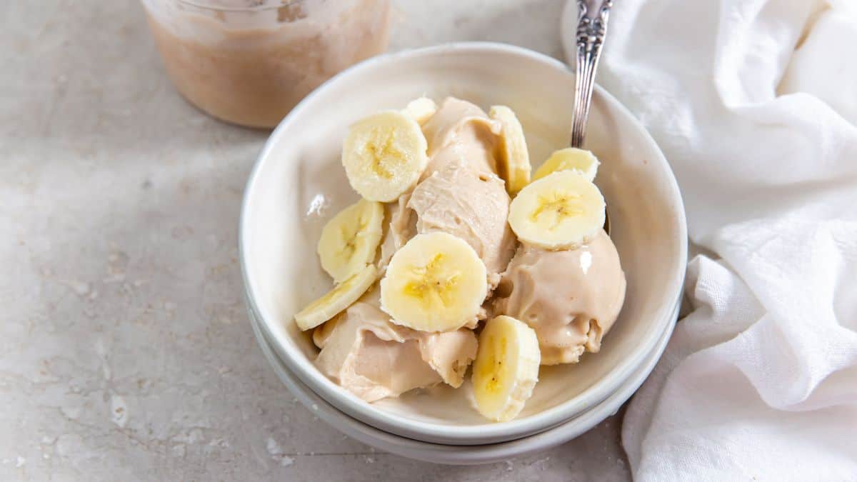 Protein Banana Ice Cream in a white bowl with a fork and bananas.