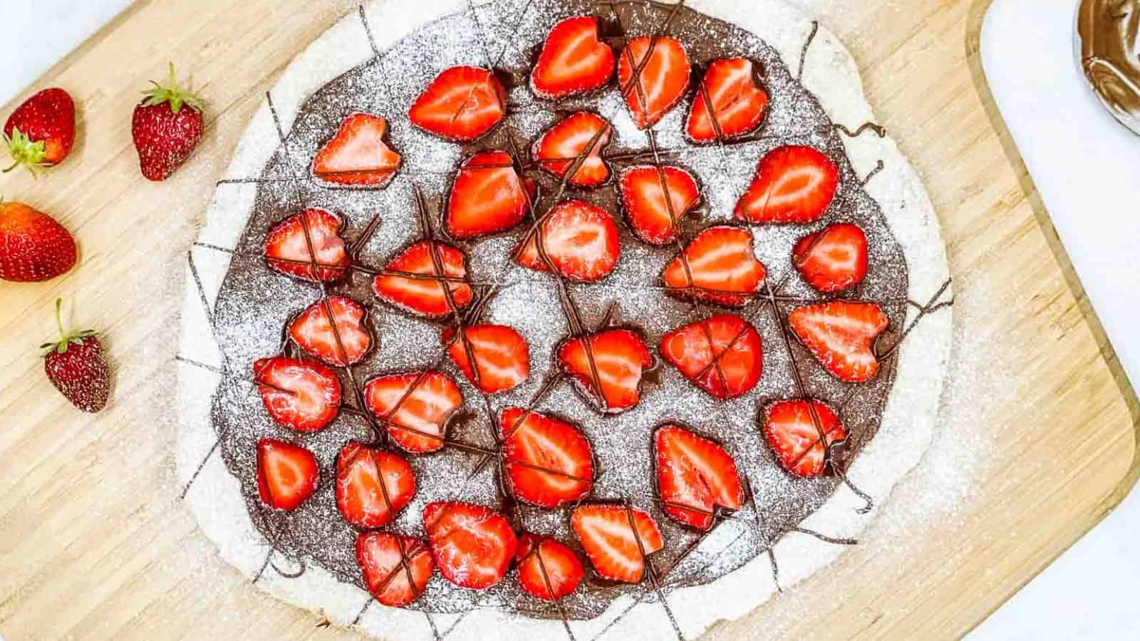 Nutella pizza with strawberries on a pizza board.