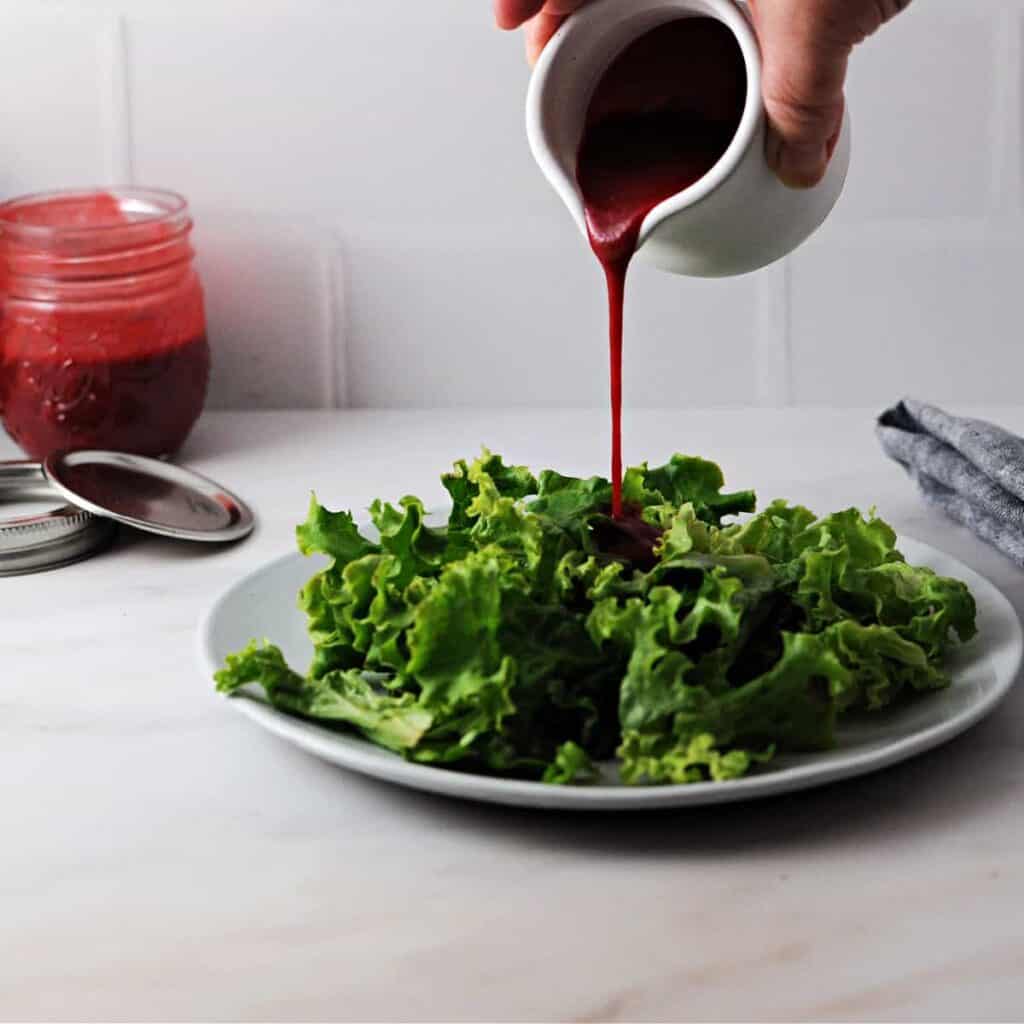 A red salad dressing being poured onto a bed of greens.