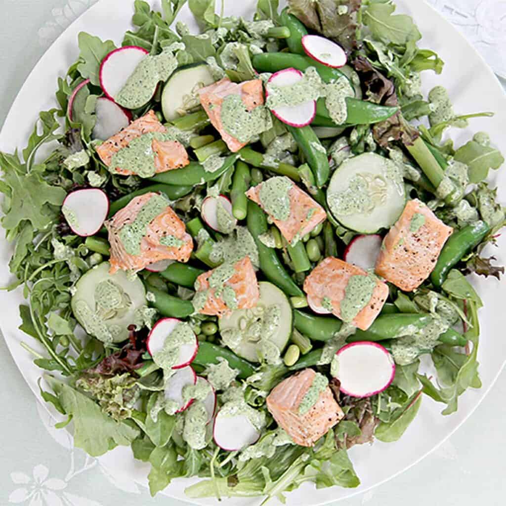 A large white plate scattered with greens, salmon and dressing.