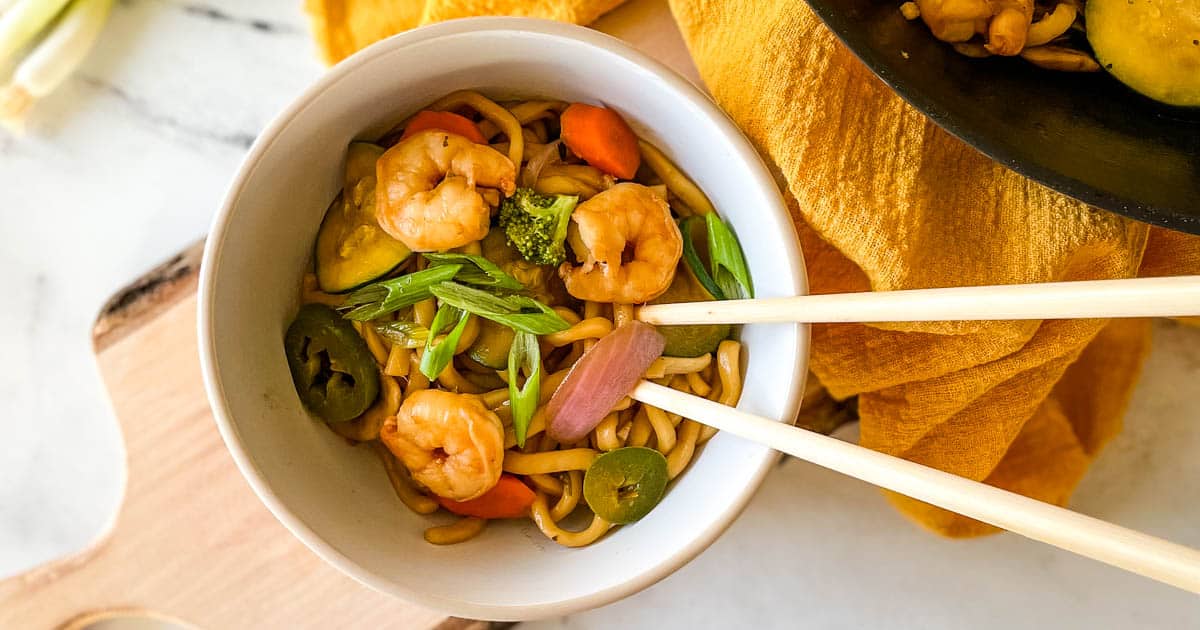 shrimp yaki udon in a white bowl with wooden chopsticks.