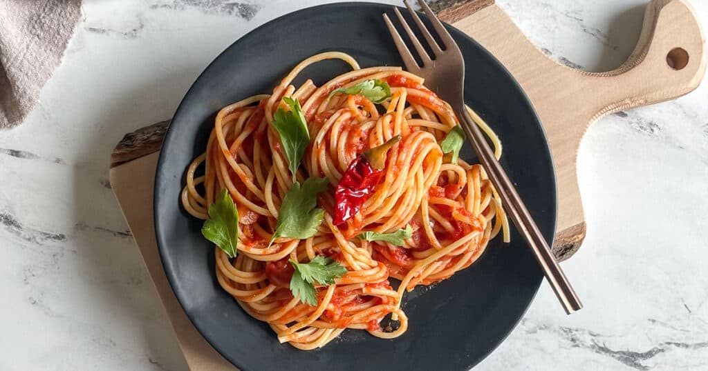 Spaghetti Arrabbiata is twirled on a black plate on a white marble counter.