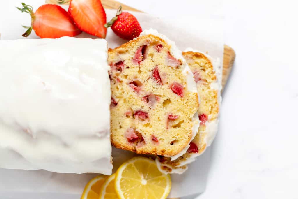 Sliced strawberry Bread on parchment paper with berries and lemons around it.