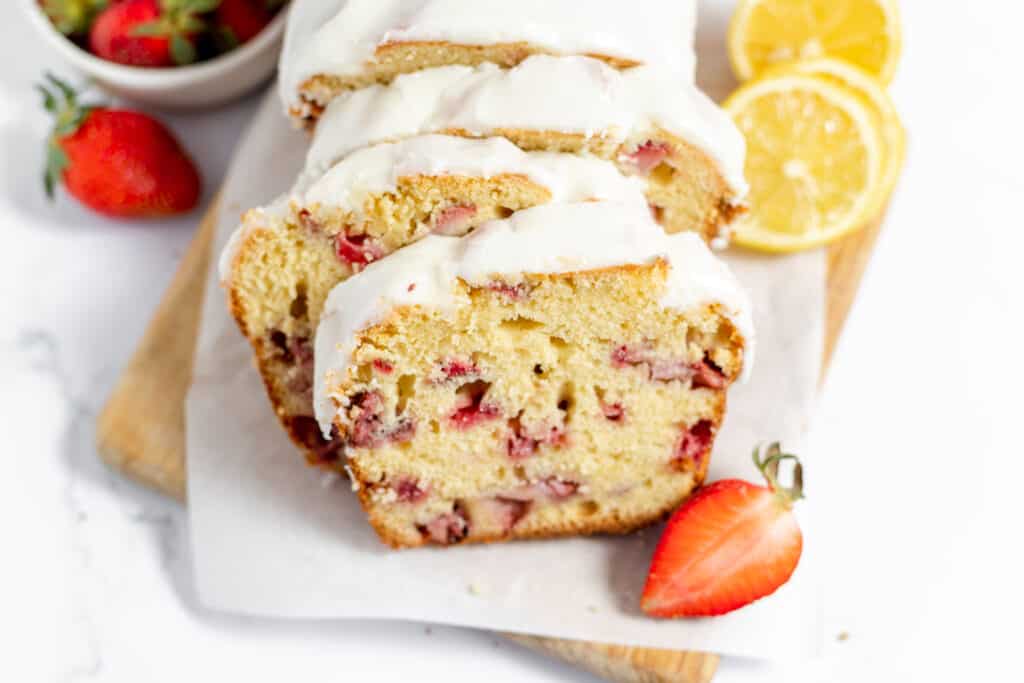 Sliced Strawberry Bread on parchment paper with berries and lemons.